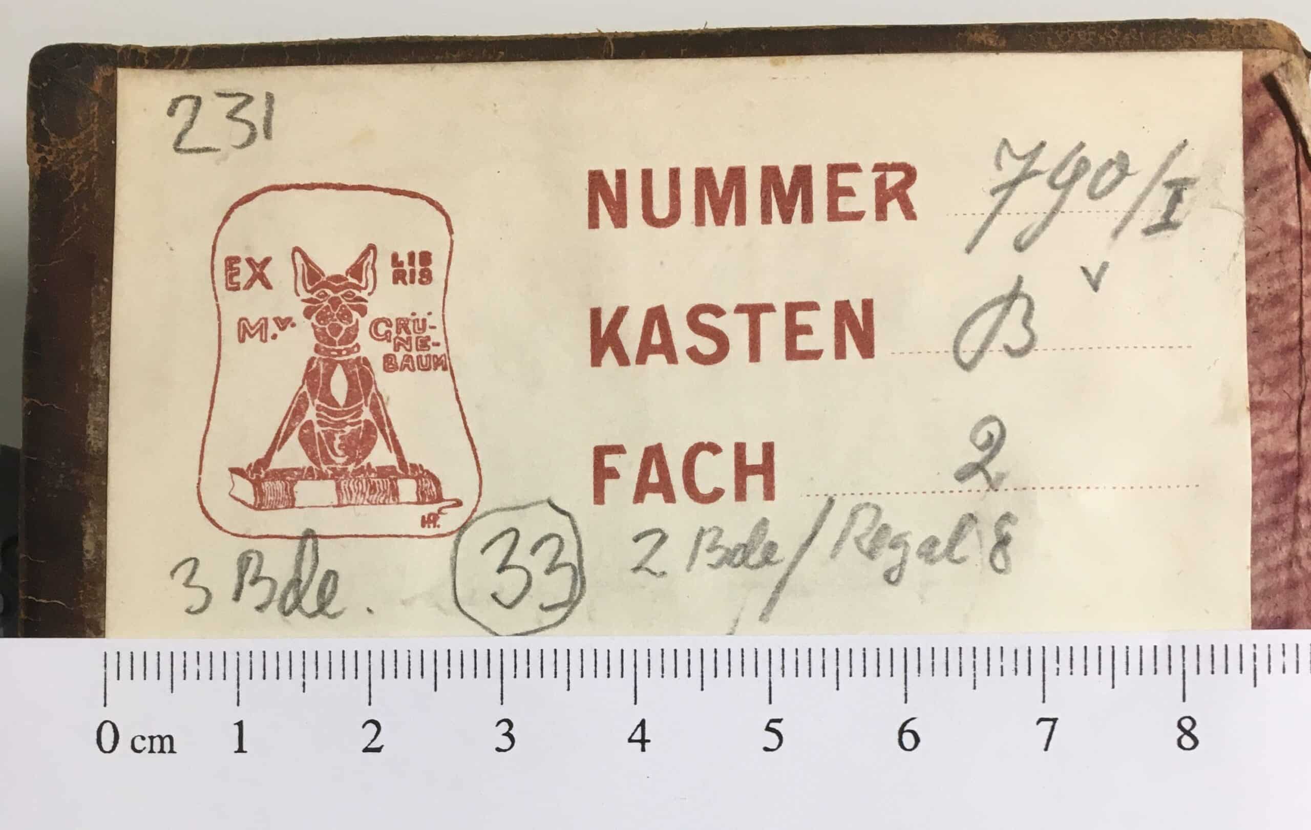 Zettel auf Bucheinband mit rotem Stempel, der eine Katze auf einem Buch sitzend zeigt und der Schriftzug: Exlibris M. v. Grünebaum